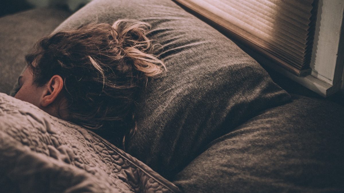 Person reading a book under soft lamp light as part of a calming pre-bed wind-down routine.